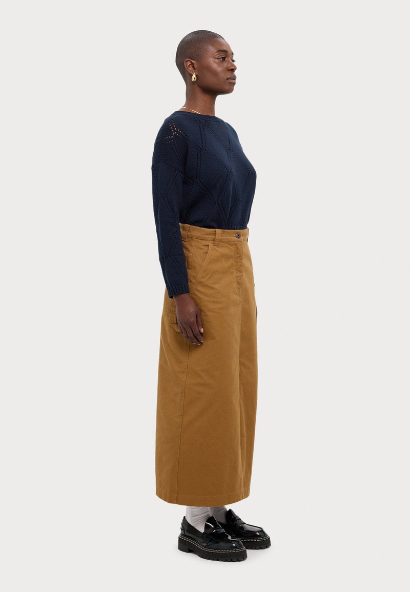 Suéter de punto azul marino con patrones geométricos, combinado con una falda de pana color beige de cintura alta y zapatos negros gruesos sobre calcetines blancos.