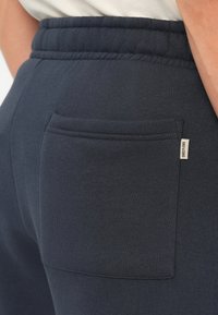 Mørkeblå joggebukser har et elastisk liv og en baklomme med et lite merke. Stoffet har en myk og jevn tekstur.