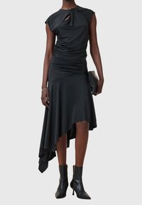 Svart klänning med kort ärm, rynkning på kroppen, asymmetrisk nederkant och en nyckelhålsöppning. Matchad med svarta ankelboots.