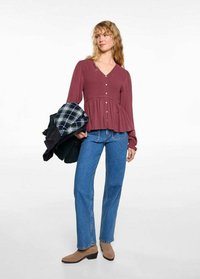 Bordeauxfarbene Bluse mit langen Ärmeln, Knopfverschluss und Peplum-Design, kombiniert mit blauen Jeans. Außerdem wird eine Jacke in Schwarz-Grün-Überprüfung gehalten.