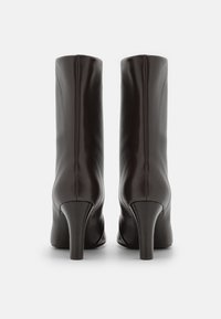 Bruna läderankelstövlar med en figurnära design, hög stilettklack, slät textur och vertikala sömmar baktill.