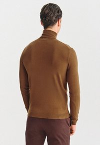Brązowy, dopasowany sweter z golfem z długimi rękawami i prążkowanym dołem, wykonany z gładkiego materiału, pokazany od tyłu.