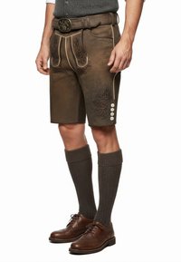 Bruine leren shorts met decoratieve borduursels, zijknopen en contrasterende bies, gecombineerd met gestructureerde kniekousen en donkere schoenen.