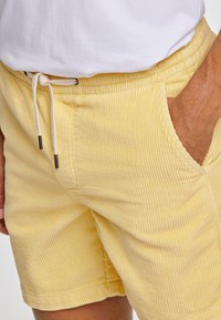 Gula kordflöjts-shorts med vertikala ränder, med dragsko i midjan och sidofickor. Slät textur och avslappnad passform.
