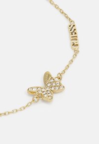 Gullfarget sommerfuglarmbånd med klare rhinestones, med kjededesign og en "Guess" logo-charms. Intrikate detaljer på sommerfuglvingene.