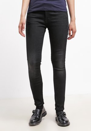 Jeans ajustados negros de denim, con una silueta entallada y un ligero desgaste en las piernas. Combinados con zapatos negros.
