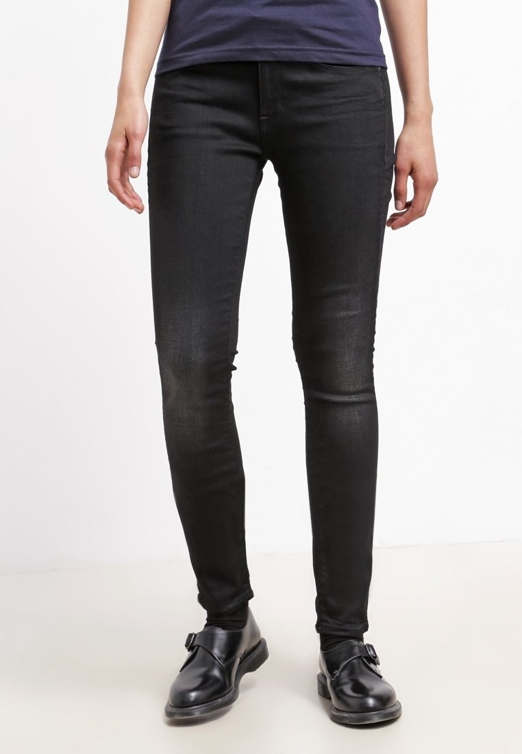 Jeans ajustados negros de denim, con una silueta entallada y un ligero desgaste en las piernas. Combinados con zapatos negros.