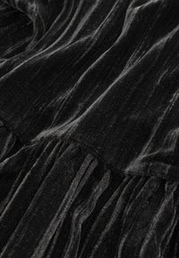 Czarna aksamitna tkanina o fakturowanym, żeberkowym wzorze z pionowymi paskami i marszczeniami wzdłuż szwu. Miękki, luksusowy wygląd.