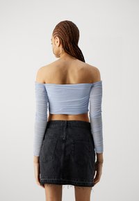 Lys blå av skulder langermet topp laget av gjennomsiktig stoff, kombinert med et kort svart denimskjørt med frynset kant og lommer.