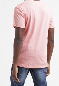 Różowa, krótko rękawowa koszulka z lekkiego materiału, z okrągłym dekoltem i luźnym krojem, widziana z tyłu. Noszona z niebieskimi dżinsami.