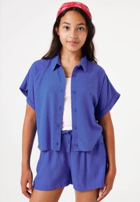 Conjunto de camisa de manga corta y pantalones cortos en tela azul sólida. Presenta un cuello y cintura ajustable con cordón. Textura suave, corte relajado.