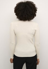Maglione in maglia a coste di un crema chiaro, con maniche lunghe, collo rotondo e silhouette aderente, caratterizzato da una leggera lucentezza e un motivo testurizzato.