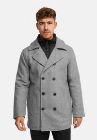 Grauener Wollmantel mit doppelreihigem Design, schwarzen Knöpfen und seitlichen Taschen, über einer schwarzen gefütterten Jacke mit Reißverschluss getragen.