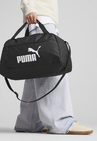Black gym bag with a durable fabric, featuring a prominent white Puma logo, two sturdy handles, and a detachable shoulder strap.