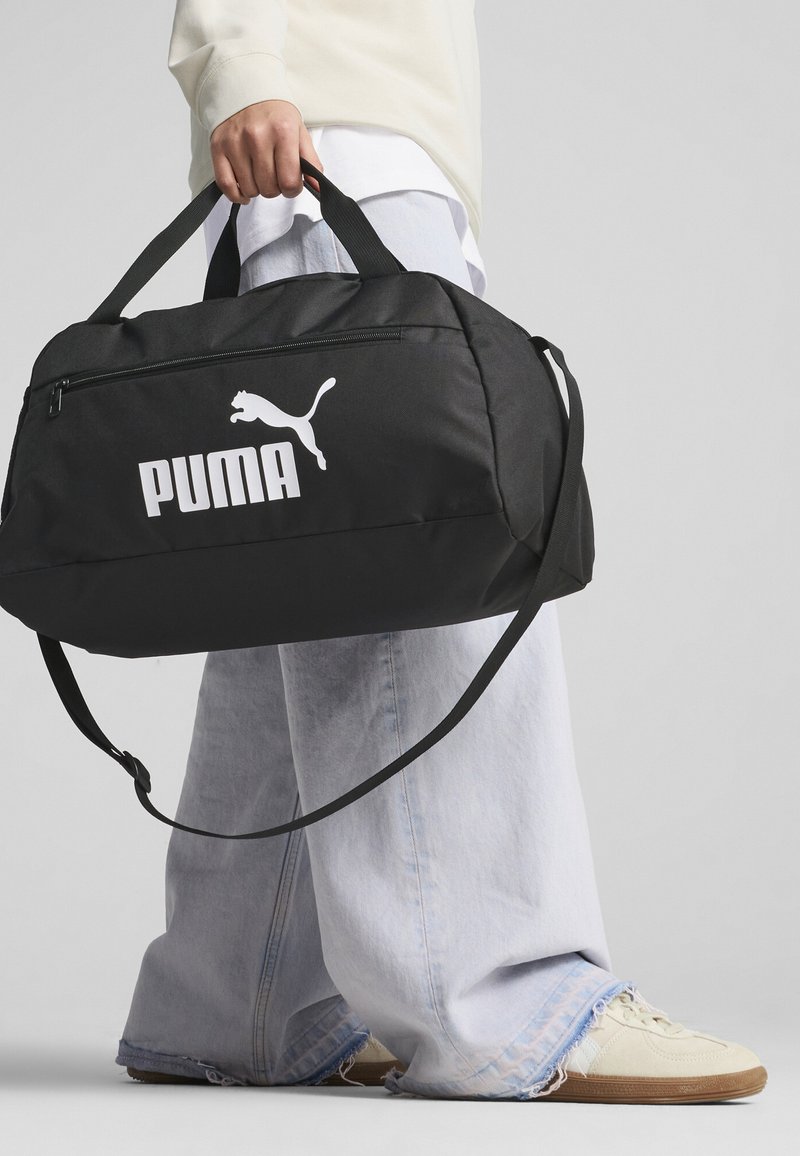Black gym bag with a durable fabric, featuring a prominent white Puma logo, two sturdy handles, and a detachable shoulder strap.