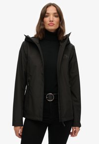 Black waterproof jacket with a zip-up front, adjustable hood, and logo patch on the chest. Smooth texture with side pockets and a fitted design.