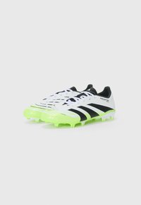 Botas de fútbol blancas con acentos negros, una parte superior texturizada y suelas de color verde neón. Presentan un cierre con cordones y una marca distintiva.