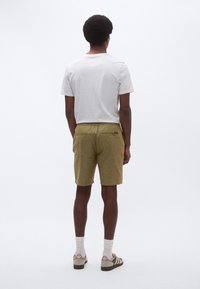 Σορτς από υφασμα με υφή σε ελιά πράσινο χρώμα με ελαστική μέση, πίσω τσέπες, συνδυασμένα με απλό λευκό T-shirt και καθημερινά παπούτσια.