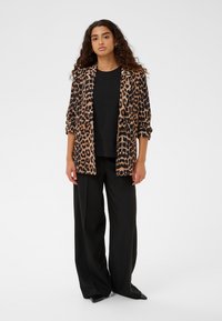 Blazer in stampa leopardata nei toni del marrone e nero, con vestibilità rilassata e maniche arrotolate, abbinato a pantaloni neri larghi e una maglietta nera attillata.