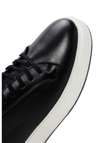 Black leather sneaker with a smooth texture, round toe, black laces, and a contrasting white sole. Features clean lines and minimal design.