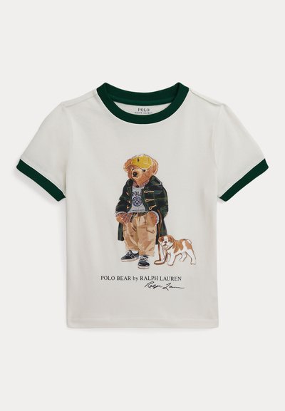 Valge t-särk rohelise soonikuga, millel on karu illustreerimine vabajas riietuses koos koeraga. All pool on tekst "POLO BEAR by RALPH LAUREN."