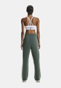 White sports bra with crisscross straps and a cutout detail; green high-waisted sweatpants, loose fit with a tapered leg.