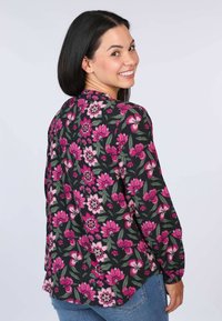 Bluse mit floralem Muster auf schwarzem Hintergrund, mit großen rosa Blumen und grünen Blättern. Lange Ärmel und entspannt geschnittener Stil.