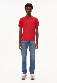 Rode T-shirt met korte mouwen, gecombineerd met lichtblauwe rechte jeans. Draagt met grijze sneakers. Eenvoudige, casual outfit zonder patronen.