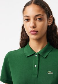 Polo vert en coton texturé, avec un col, deux boutons blancs et un petit logo brodé sur la poitrine gauche.
