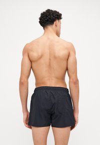 Shorts de bain noirs en matériau léger, dotés d'une taille élastique, d'une poche arrière et d'un design simple sans embellissements.