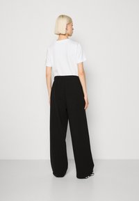 Pantaloni da cerimonia neri a gamba larga con vita elastica, abbinati a una semplice t-shirt bianca a maniche corte. Design semplice e minimal.