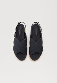 Sandalias slingback de lona azul marino con tiras entrelazadas, suelas de goma y detalle de hardware dorado. Plantilla texturizada para mayor comodidad.