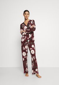 Floral pajama set in burgundy, featuring a button-up shirt with long sleeves and matching pants with a relaxed fit, adorned with large white flowers.