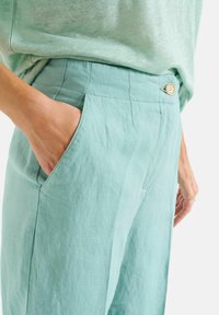 Lichtblauwe linnen broek met een ontspannen pasvorm, voorzien van zijzakken en een enkele knoopsluiting. Zachte textuur en minimalistisch ontwerp.