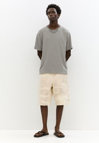 Šedé oversized tričko s hrubými okraji, krémové šortky s jemnou texturou a černé žabky. Jednoduchý, ležérní vzhled.