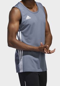 Šedý sportovní tílko s bílým logem Adidas a třemi vertikálními bílými pruhy po stranách. Lehký, prodyšný materiál, bez rukávů.