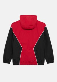 Κόκκινο και μαύρο αδιάβροχο μπουφάν με κουκούλα, που διαθέτει γεωμετρικό σχέδιο, ελαστικούς σφιγκτήρες στους καρπούς και λευκή ραφή κατά μήκος των ραφών.