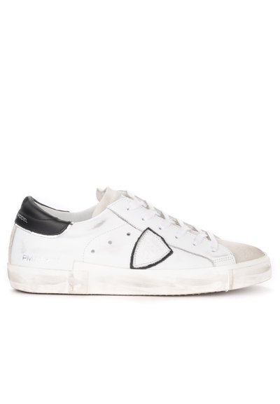 Sneaker bianco in pelle con accentuazione nera sul tallone. Presenta chiusura con lacci, logo triangolare e suola intermedia texturizzata. Aspetto usurato.