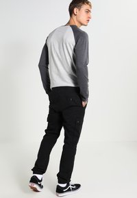 Camicia a maniche lunghe con corpo grigio e maniche grigio scuro, abbinata a pantaloni cargo neri. L'outfit presenta una vestibilità slim e un design semplice. Sneakers nere completano il look.