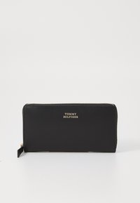 Melna ādas maciņš ar zelta toņu detaļām. Ar rāvējslēdzēja aizdari un iegrieztu zīmola logo. Gluda tekstūra un taisnstūra forma.