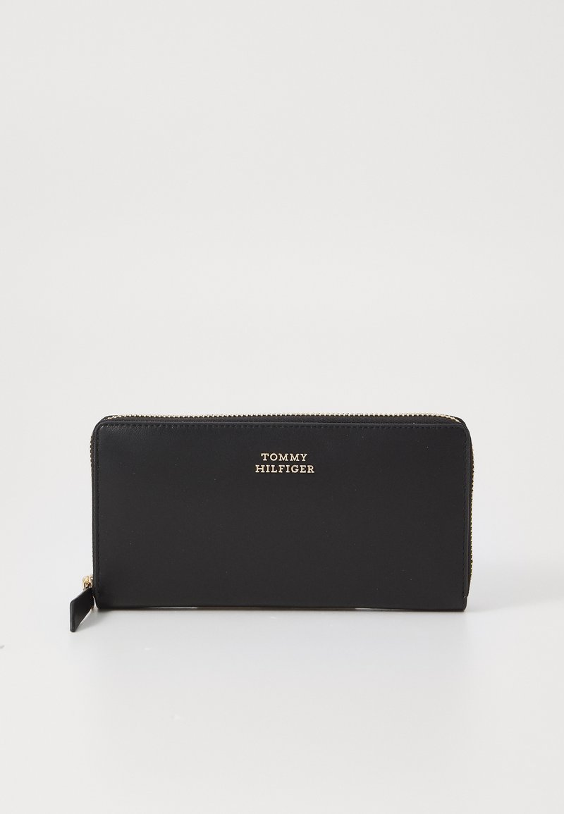 Melna ādas maciņš ar zelta toņu detaļām. Ar rāvējslēdzēja aizdari un iegrieztu zīmola logo. Gluda tekstūra un taisnstūra forma.