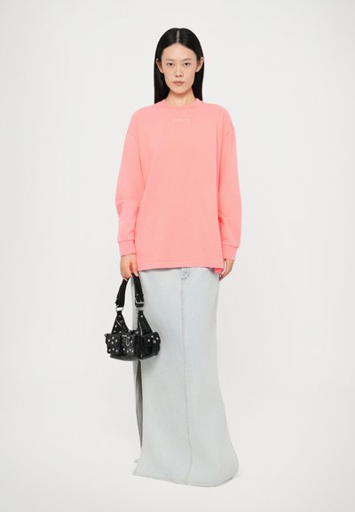 Oversized neon pink sweatshirt with "STIEGLITZ" text, paired with a light denim maxi skirt and a small black structured handbag.
