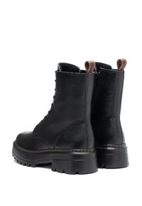 Une paire de bottes de combat en cuir noir à lacets avec des semelles épaisses et des tirants en cuir marron, montrées sous des angles arrière.