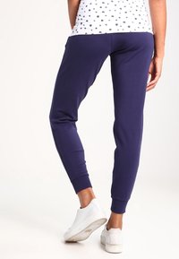 Námořnické modré tepláky s žebrovanými manžetami, měkkou tkaninou a těsným střihem. Nosené s bílými teniskami, které mají hladký povrch a minimalistický design.