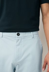 Vaaleansiniset rennot housut, joissa on musta nappikiinnitys ja suora etumalli. Sileä pinta, vähäiset saumauskohdat.