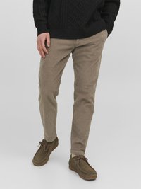 Pantaloni in corduroy beige con righe orizzontali, abbinati a scarpe scamosciate marroni scure. L'outfit presenta un maglione lavorato nero testurizzato.