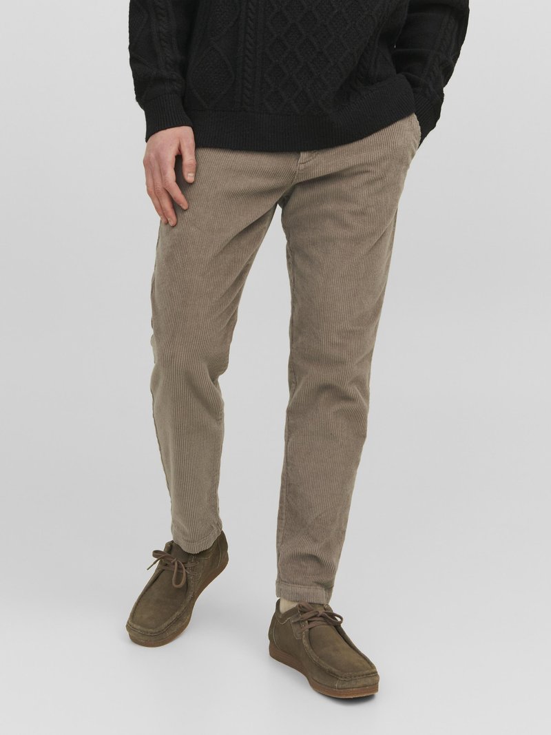 Pantaloni in corduroy beige con righe orizzontali, abbinati a scarpe scamosciate marroni scure. L'outfit presenta un maglione lavorato nero testurizzato.