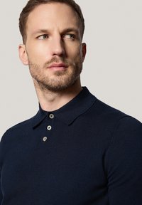 Granatowa koszulka polo z fakturowanej tkaniny, z krótkimi rękawami i zapięciem na trzy guziki. Posiada klasyczny kołnierzyk, co zapewnia schludne wykończenie.