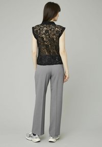 Top en dentelle noire avec motif floral et manches courtes, associé à un pantalon large gris et des baskets avec accents argentés.