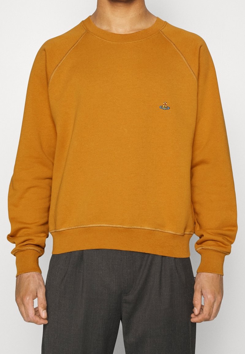 Sudadera de color mostaza hecha de algodón, con un cuello redondo, mangas raglán y un pequeño diseño bordado en el pecho.